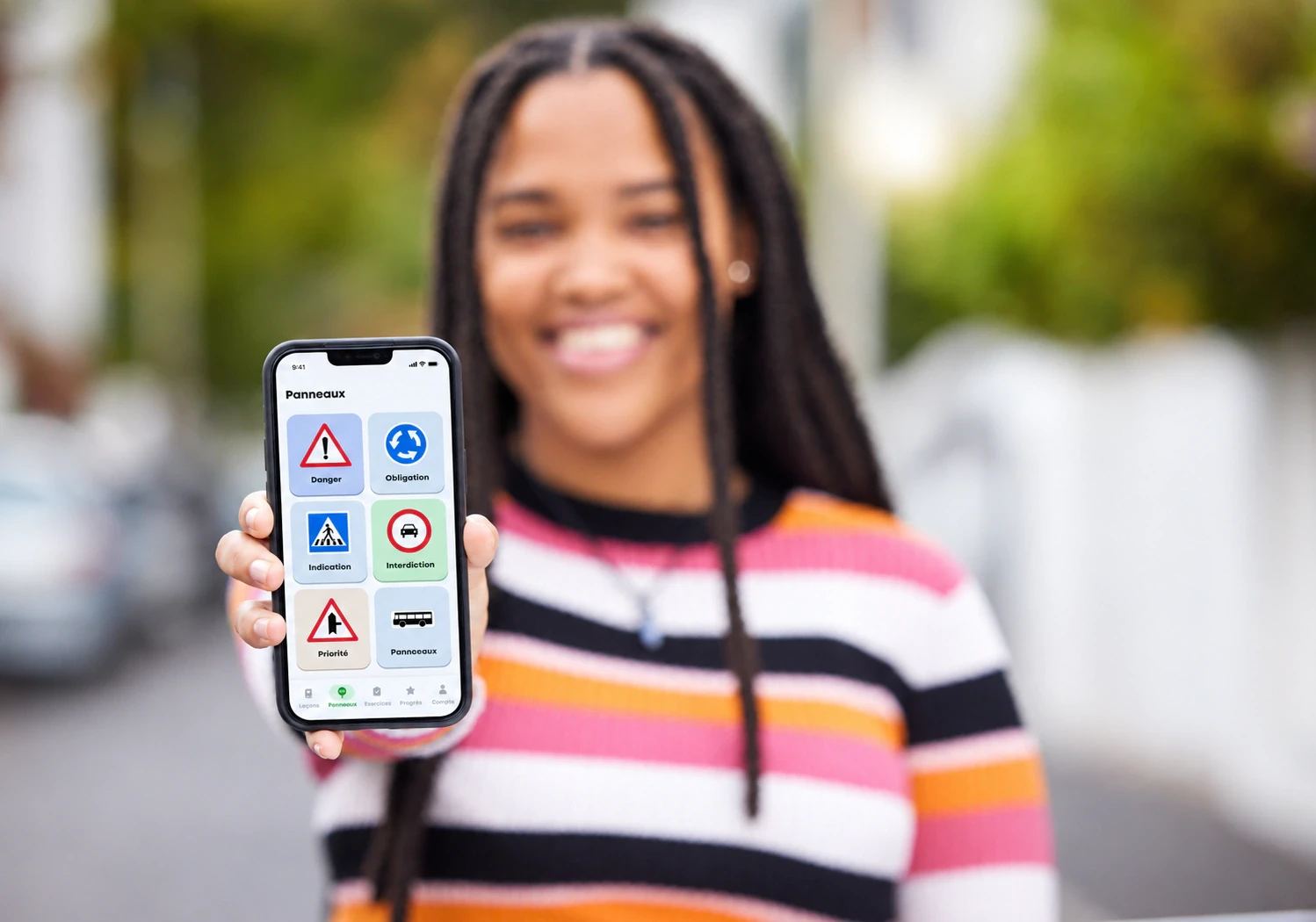 Une élève souriante montre l'écran Panneaux de l'application e-Moniteur sur son téléphone